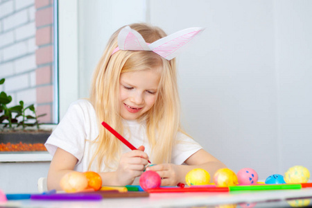 小女孩戴着兔子耳朵在头上准备复活节和画鸡蛋。 五颜六色的标记。 复活节和假日的概念。