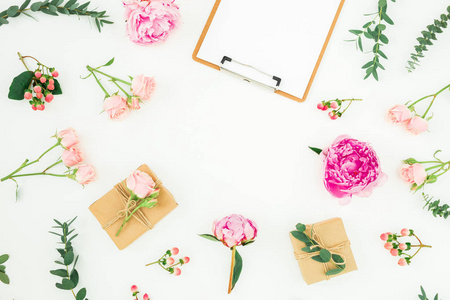 花架粉红色牡丹，玫瑰，金丝桃和桉树与剪贴板和礼物在白色背景。平躺，俯视