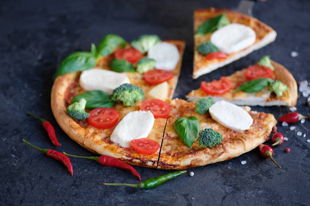 切片比萨饼与莫扎雷拉奶酪，西红柿，西兰花，香料和新鲜罗勒。 意大利披萨。 黑石背景披萨