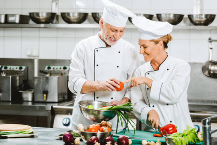 微笑的男女厨师穿着双胸夹克和帽子在餐厅厨房做饭