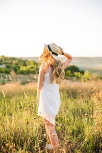 阳光明媚的一天，在夕阳下的田野里，一个可爱的年轻女孩，金发碧眼，穿着白色的太阳裙，戴着草帽