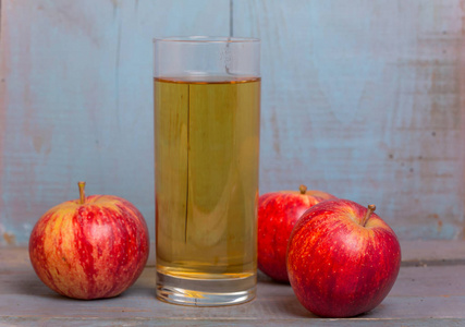 一杯苹果汁和一个红苹果放在一个蓝色的旧木制背景上