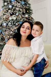 美丽的母亲和儿子在圣诞树附近的沙发上