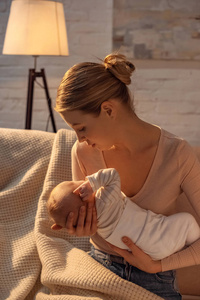 年轻母亲坐在沙发上，晚上哺乳时抱着新生婴儿