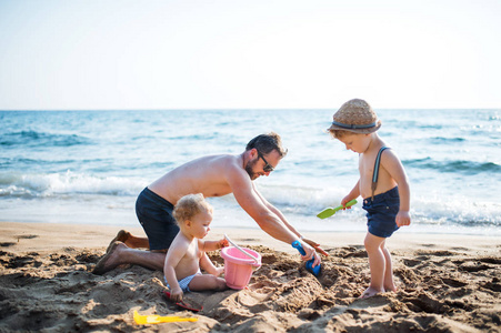 暑假里, 父亲带着两个幼儿在海滩上玩沙子