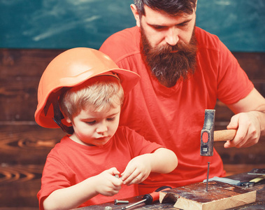 父亲, 父母用胡子教小儿子用 hobnails 和锤子。男孩, 孩子忙着保护头盔学习锤击 hobnails 与爸爸。车间和杂工概