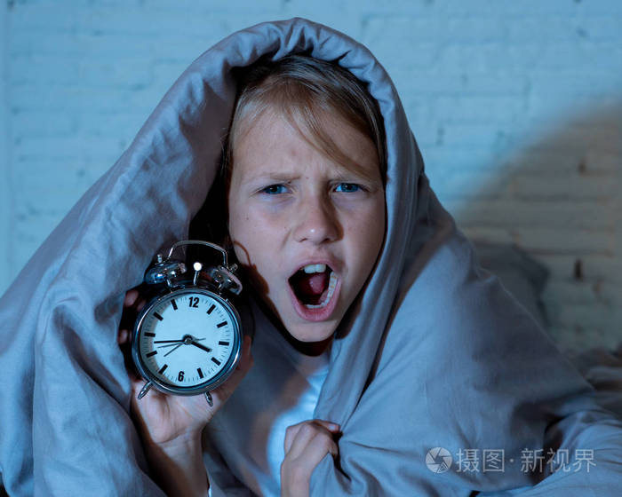 可爱的失眠小女孩躺在床上闹钟看起来很累有睡眠问题晚上睡觉或者在