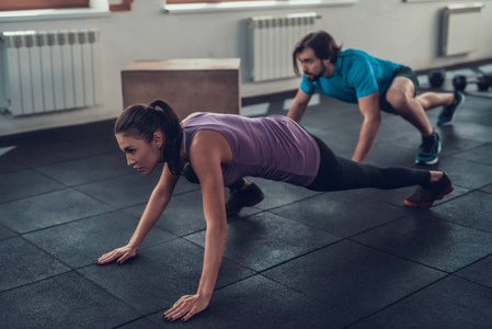 穿紫色T恤的女孩。 训练日。 健身俱乐部。 健康的生活方式。 强大的运动员。 活跃的假日。 交叉的概念。 健身房地板爬行。 舒适
