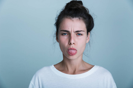 一个不高兴的年轻女人，穿着T恤，被蓝色背景隔离，伸出舌头