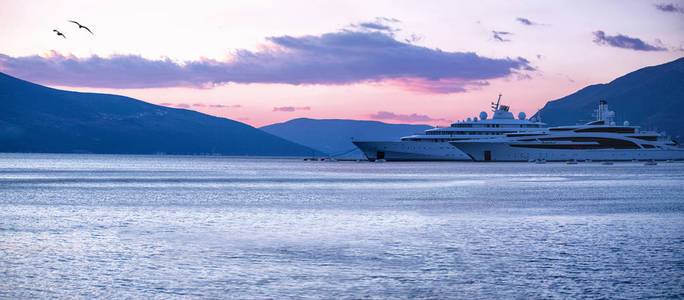 豪华超级游艇在码头与山的轮廓在粉红色日落波尔图蒙登纳戈宽全景