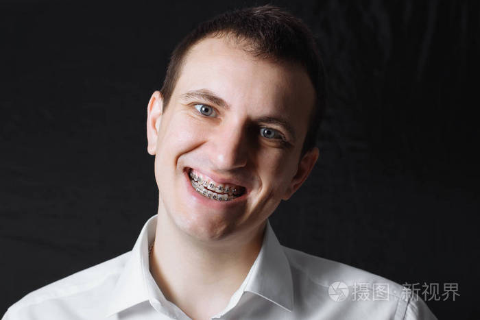 一个白种人的肖像,他的牙齿上戴着一件黑色背景的白色衬衫,牙齿上戴着
