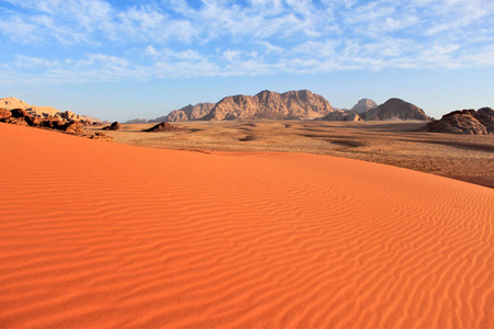 约旦的瓦迪朗姆沙漠。 大面积，光滑的未触及的红色沙子和山脉的背景和蓝天与云。