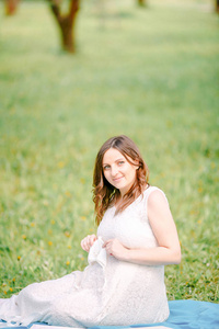 穿着白色连衣裙坐在草地上微笑的怀孕女孩