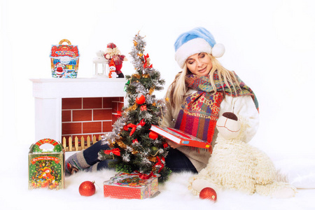 圣诞前夜，在圣诞树附近，带着壁炉糖果和玩具的蓝帽子和白毛衣的快乐女人