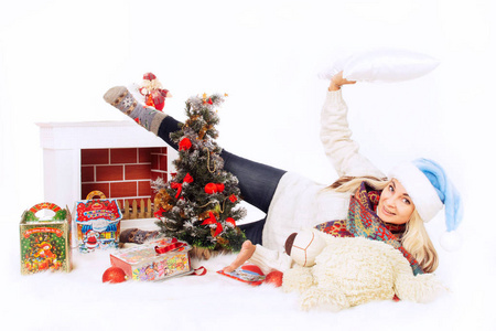 圣诞前夜，在圣诞树附近戴着蓝色帽子和白色毛衣的快乐女人带着壁炉糖果和玩具