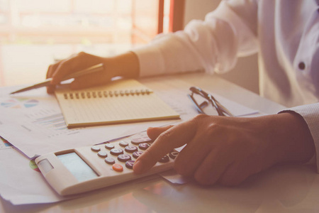 一个人用一个带笔记的财务计算器，在家里的办公桌上分析财务数据