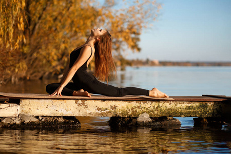 年轻女子在秋天公园的安静码头练习瑜伽。