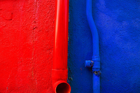 一座典型的博拉诺岛房子的墙被分成两半，涂上了明亮的红色和蓝色。 排水沟的细节和与墙壁颜色匹配的管道。 意大利
