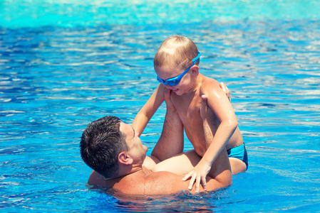 父亲和儿子在夏日的阳光下在游泳池里跳跃和游泳。 假日休闲和游泳。
