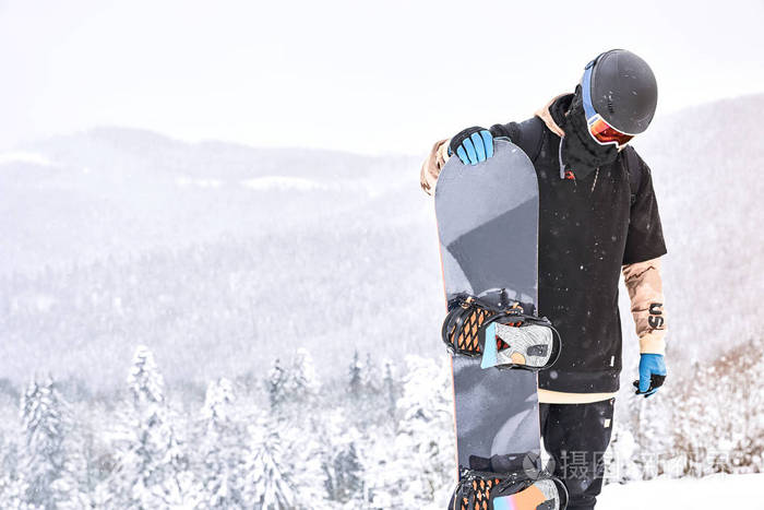 男雪衣员在山顶上看着他的滑雪板,背景上有山和休息