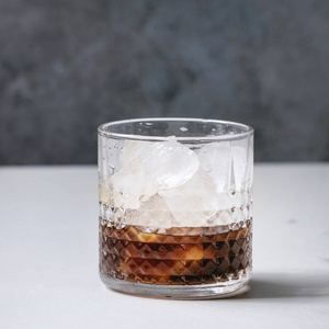 冰咖啡鸡尾酒或碎冰，玻璃中的冰块在白色大理石桌子上，背景是灰色混凝土墙。 正方形图像