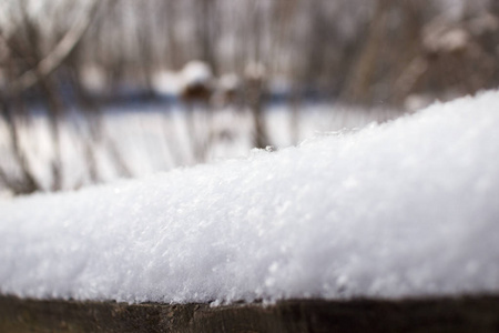 在冬天，毛茸茸的雪在阳光下闪闪发光。雪躺在木栅栏上，在背景上有一个美丽的波克。雪片关闭