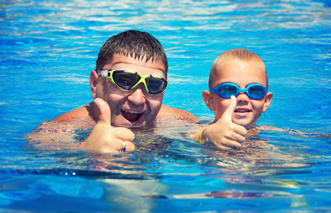 父亲和儿子在夏日的阳光下在游泳池里跳跃和游泳。假期休闲和游泳..