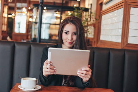 美丽迷人的黑发微笑的亚洲女孩与平板电脑桌上的咖啡馆学生自由职业者或年轻经理