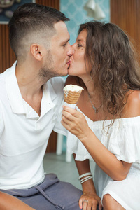 年轻的白色接吻夫妇坐在咖啡馆里。拿着冰淇淋蛋筒的女孩