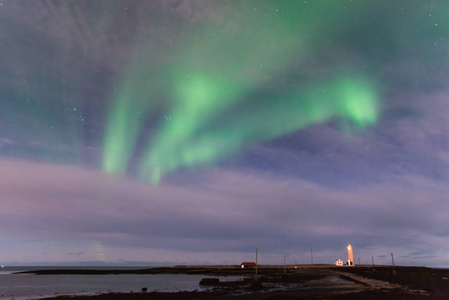 冰岛石窟灯塔上的绿色北极光，前景是海洋和黑色沙滩