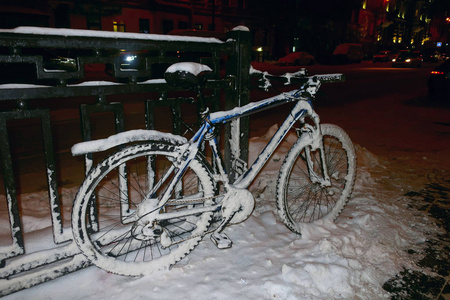 一辆雪覆盖的自行车停在冬天的街道上的篱笆上。