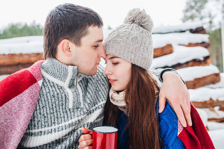 年轻的浪漫夫妇与热饮料在冬季森林。恋爱中的一对