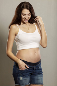 怀孕和期望概念快乐孕妇，触摸她的腹部灰色背景垂直肖像
