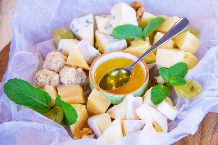 白纸上有不同类型奶酪的盘子，用绿色薄荷叶装饰的蜂蜜