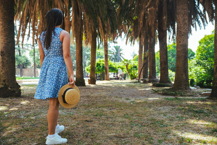 穿着蓝色衣服在棕榈公园散步的女人。 暑假假期