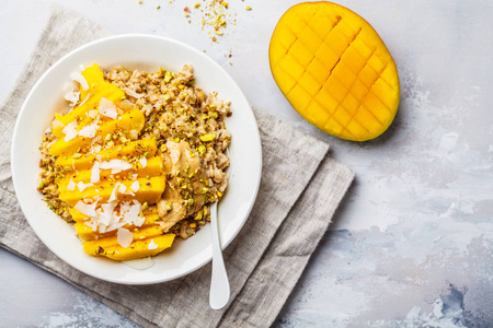 燕麦粥与芒果椰子花生酱和坚果在白色盘子顶部视图。 素食健康早餐植物的概念。