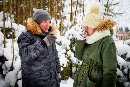 一个冬天，男孩和女孩在雪林里散步。 青少年在周末户外喝茶。 在下雪的公园里，人们在寒冷的日子穿着暖和的衣服