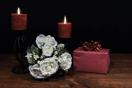 美丽的花束，红色蜡烛放在一个支架上，一个礼物放在一张木桌上。 母亲节复活节情人节生日圣诞节