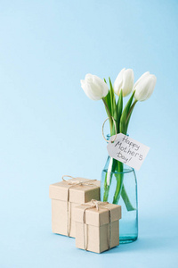 礼品盒和白色郁金香花束，蓝色背景上有快乐的母亲节问候标签