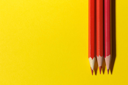 三支红色铅笔在明亮的黄色背景上。 文本的地方。 上文视