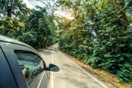 夏季在森林公路上行驶的黑色汽车的侧视图。 旅行和探索概念。