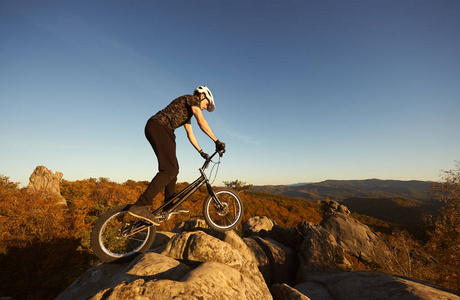 年轻的男性骑自行车在大巨石上的试骑自行车上平衡