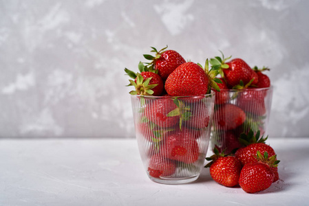 红色成熟草莓在玻璃碗灰色混凝土桌背景复制空间。 健康食品概念