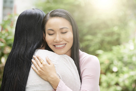 成年亚洲女人拥抱成熟的母亲，眼睛紧闭，阳光明媚