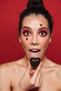 美丽的肖像，一个美丽的年轻无胸女子，化妆，站在红色背景上，手持心形巧克力糖果