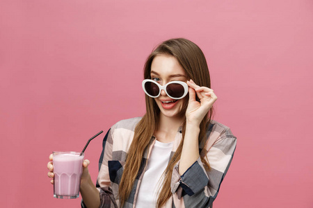一个可爱的休闲女孩的肖像，从一个玻璃喝橙汁，看着相机隔离在粉红色的背景。
