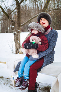 冬天，母女俩坐在树林里的长凳上