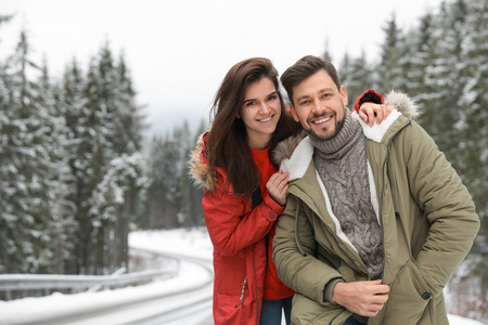 一对夫妇穿着温暖的衣服雪林空间附近发短信。 寒假