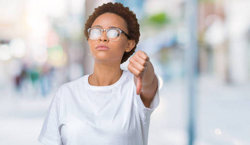 美丽的年轻非洲裔美国妇女戴着眼镜，在孤立的背景上看起来不高兴和愤怒，表现出拒绝和消极的拇指向下的手势。 不好的表情。
