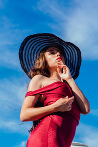 美丽的年轻女子在红色礼服和巴拉克帽子在夏天阳光明媚的天在蓝天背景